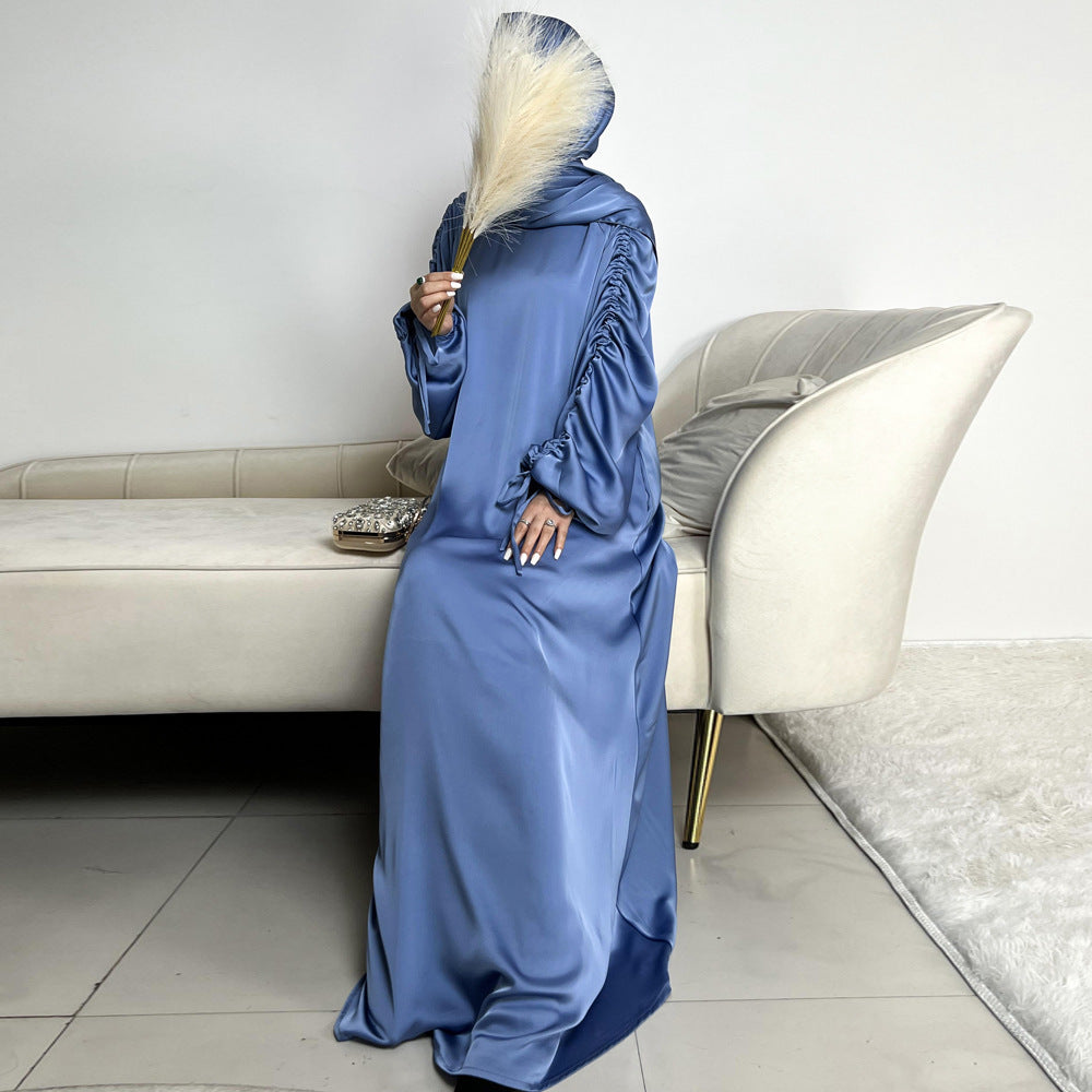 Élégance satinée, féminité affirmée. Cette abaya en tissu satiné ultra chic met en valeur la silhouette avec des manches froncées modernes et une finition fluide