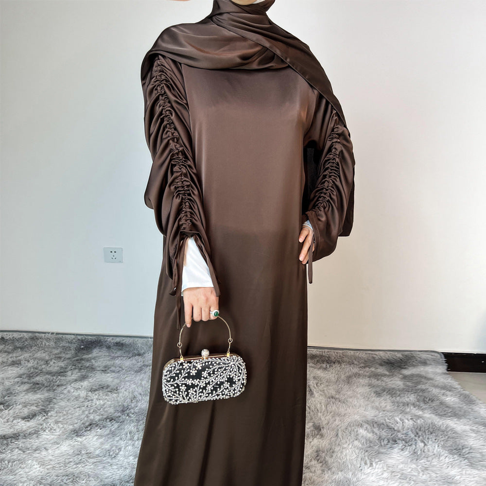 Élégance satinée, féminité affirmée. Cette abaya en tissu satiné ultra chic met en valeur la silhouette avec des manches froncées modernes et une finition fluide