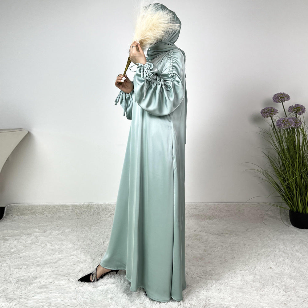 Élégance satinée, féminité affirmée. Cette abaya en tissu satiné ultra chic met en valeur la silhouette avec des manches froncées modernes et une finition fluide