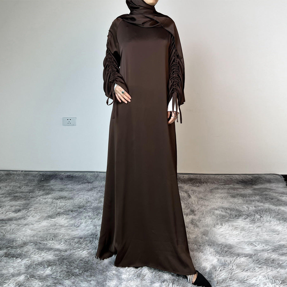Élégance satinée, féminité affirmée. Cette abaya en tissu satiné ultra chic met en valeur la silhouette avec des manches froncées modernes et une finition fluide