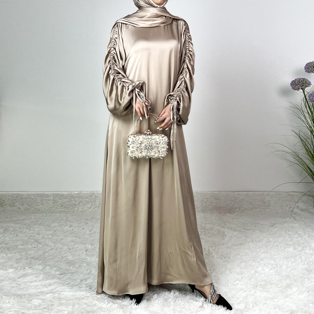 Élégance satinée, féminité affirmée. Cette abaya en tissu satiné ultra chic met en valeur la silhouette avec des manches froncées modernes et une finition fluide