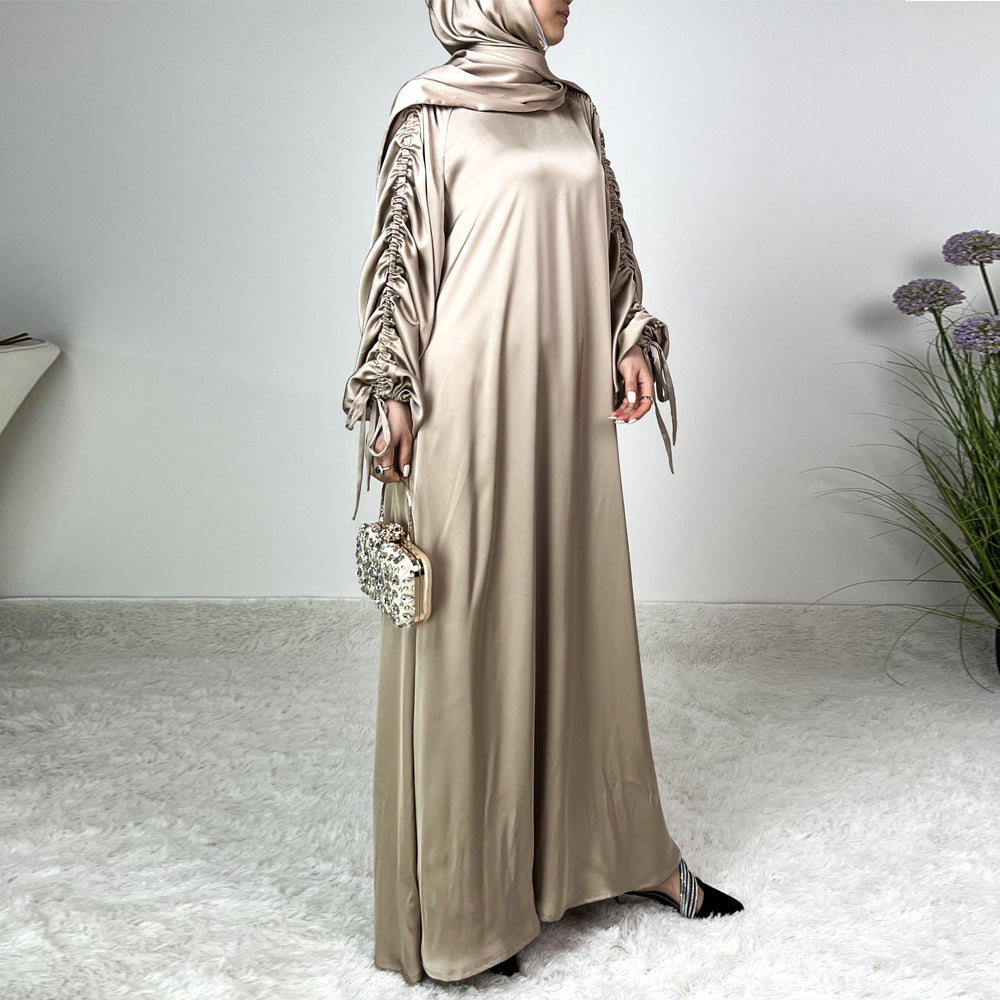 Élégance satinée, féminité affirmée. Cette abaya en tissu satiné ultra chic met en valeur la silhouette avec des manches froncées modernes et une finition fluide