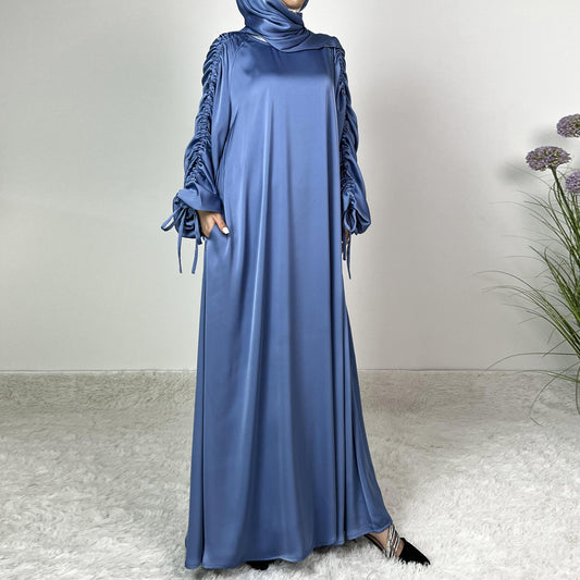 Élégance satinée, féminité affirmée. Cette abaya en tissu satiné ultra chic met en valeur la silhouette avec des manches froncées modernes et une finition fluide